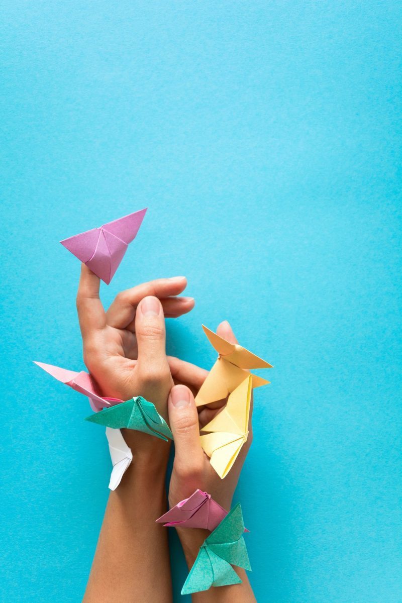 hands holding several paper birds against blue background